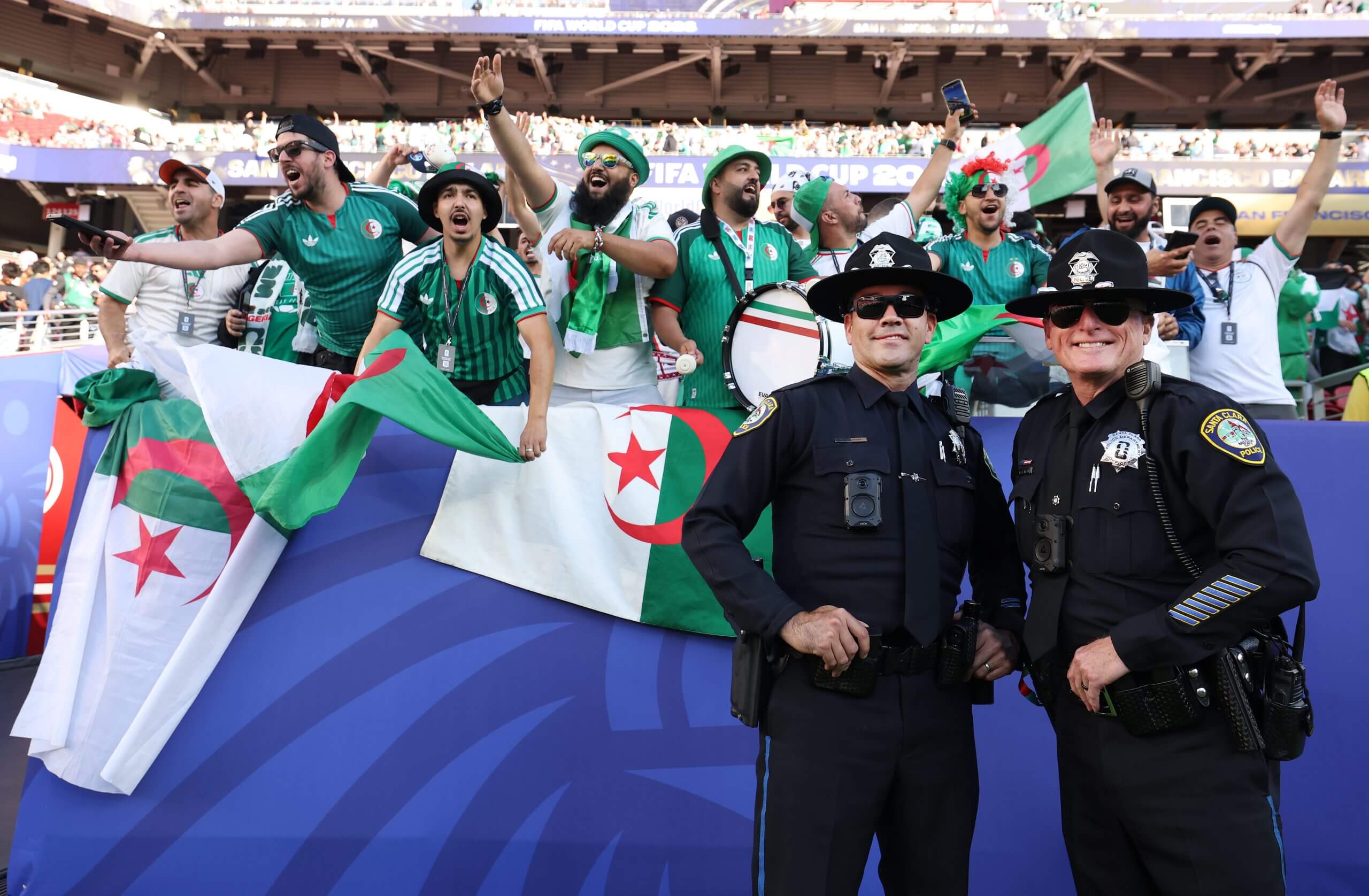 Police officers pose for photos as Algeria fans cheer in the stands
